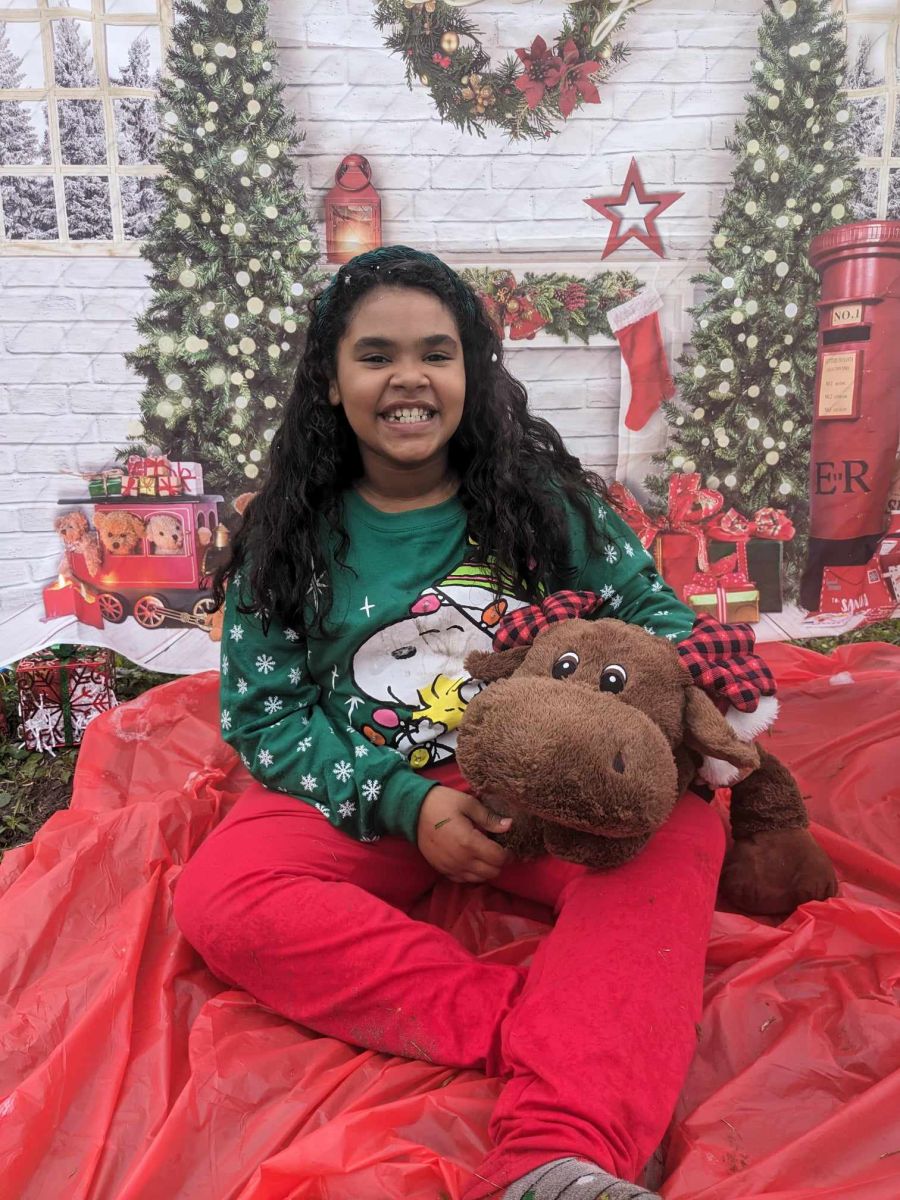 girl holding stuffed animal in front of christmas trees